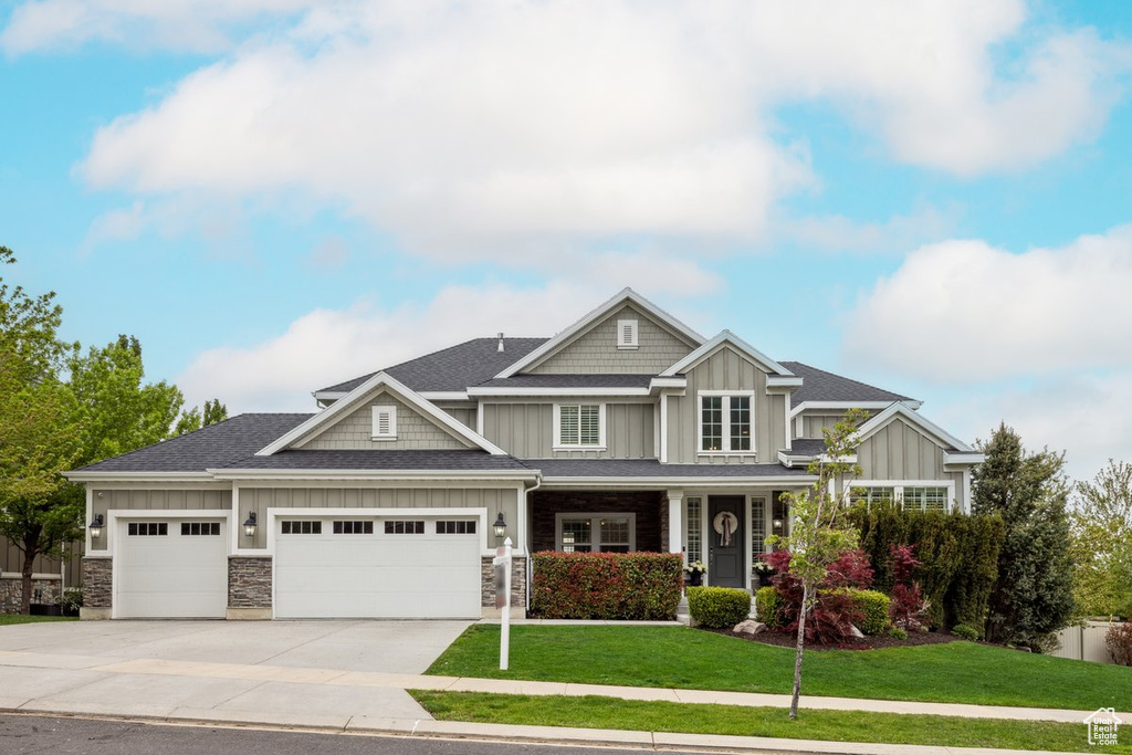 Craftsman-style home with board and batten siding, a garage, a front lawn, and stone siding