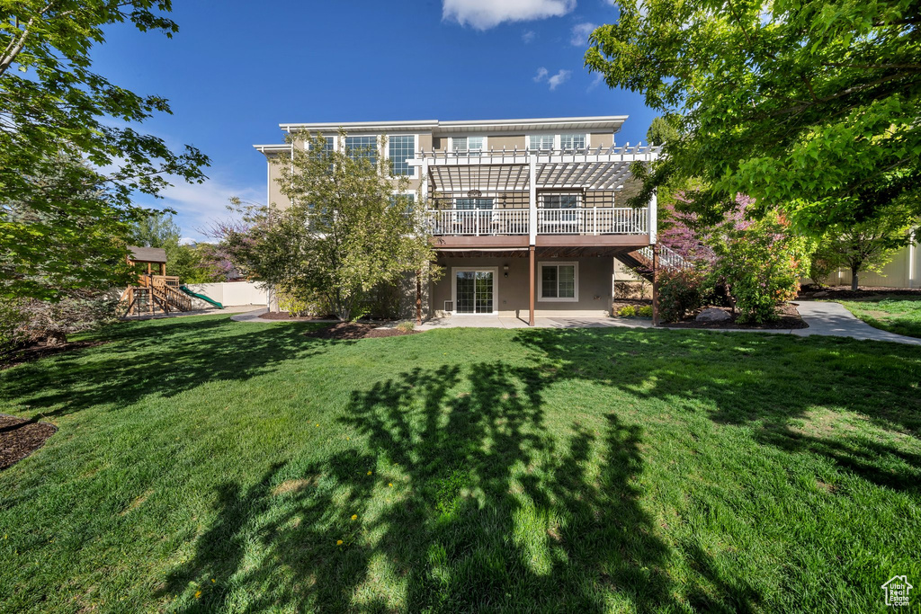 Rear view of house with a pergola, a patio area, a yard, a playground, and a wooden deck