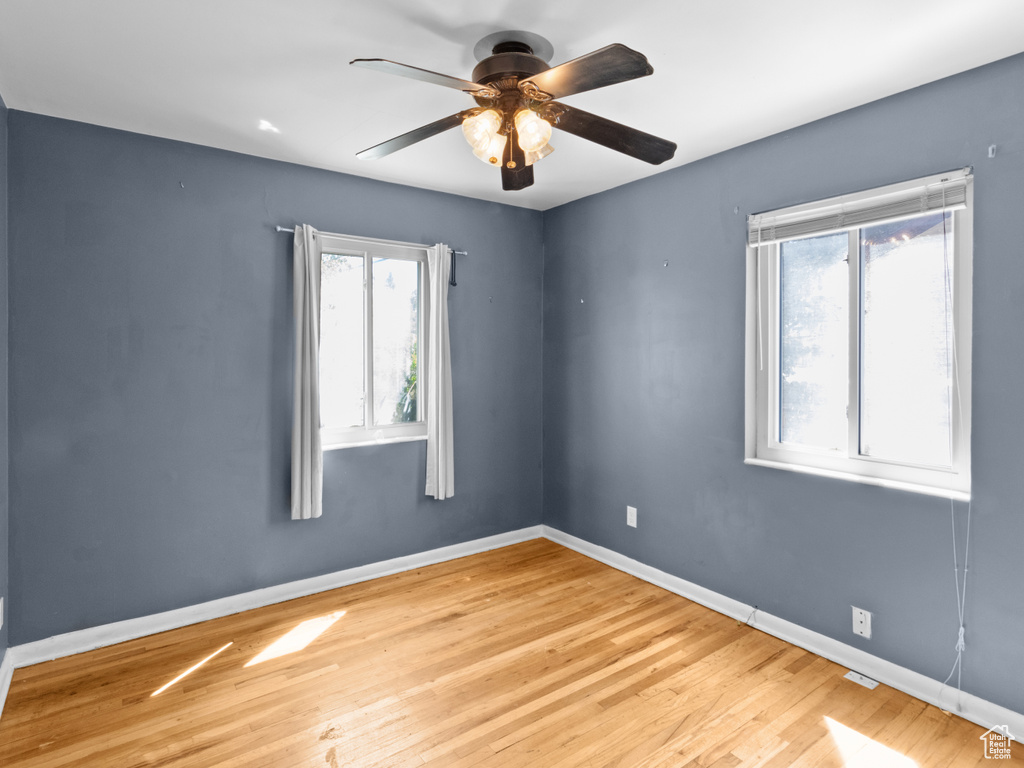 Unfurnished room featuring healthy amount of natural light, wood finished floors, baseboards, and a ceiling fan