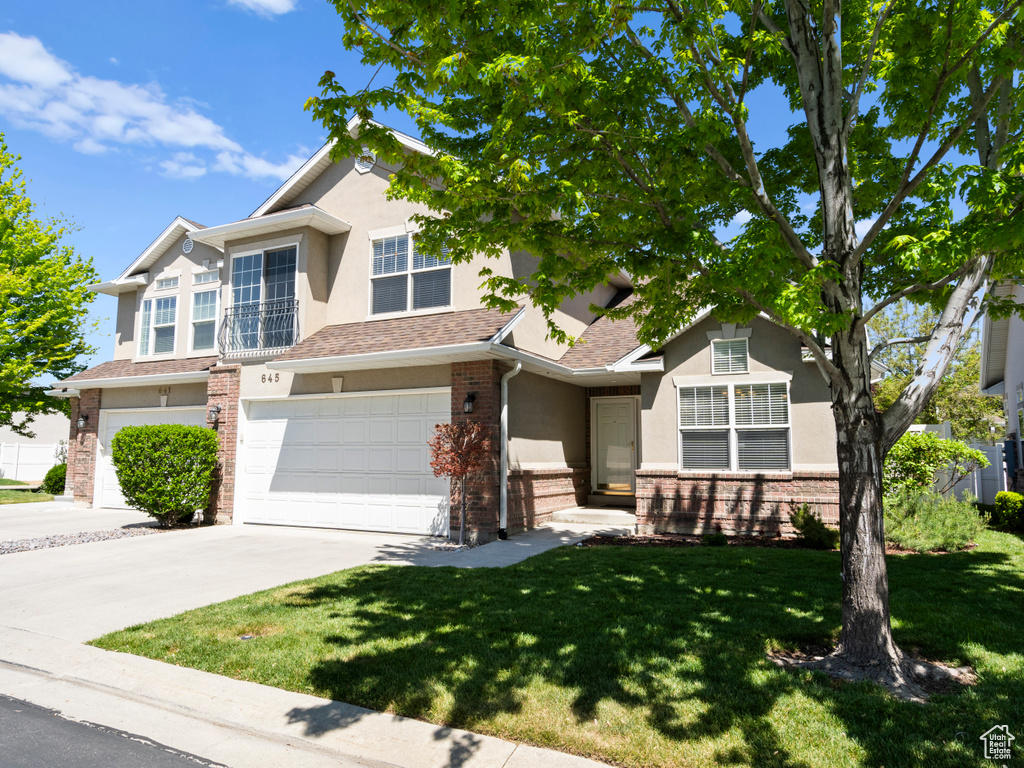 View of front of property featuring stucco siding, driveway, brick siding, a front yard, and an attached garage