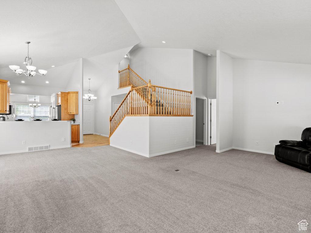 Unfurnished living room featuring a chandelier, light carpet, recessed lighting, high vaulted ceiling, and stairway