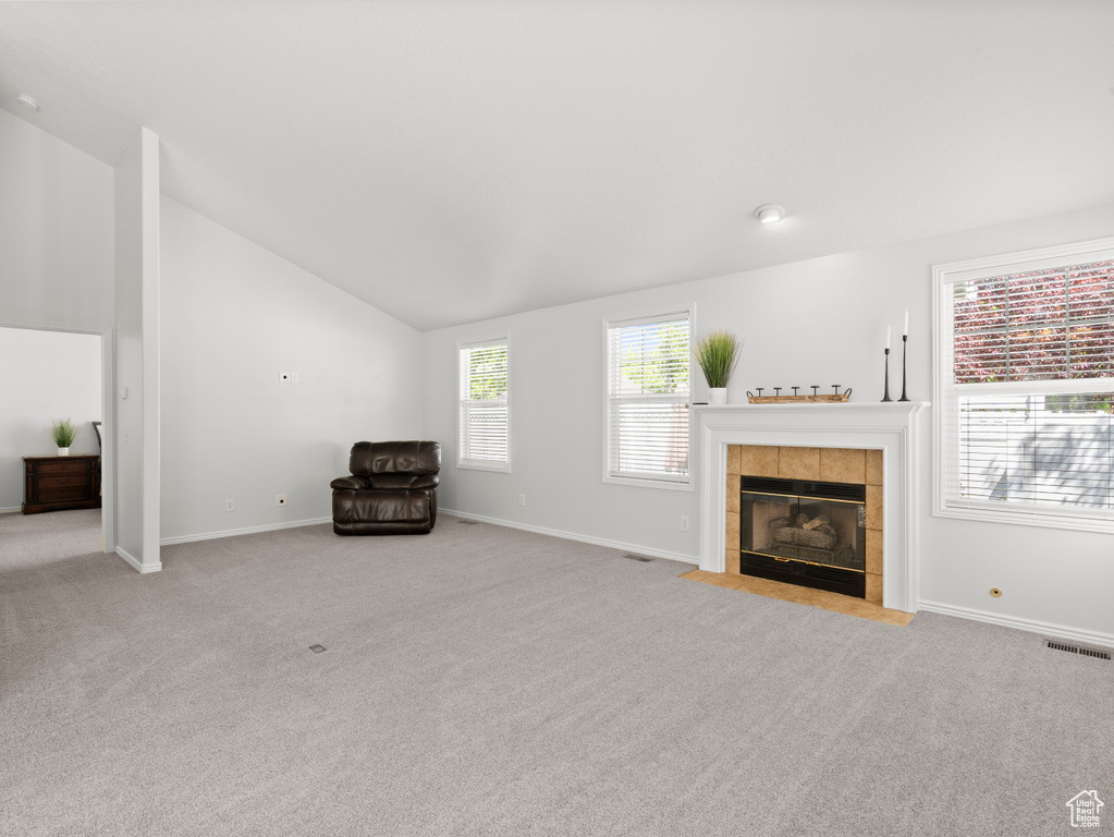 Unfurnished room featuring carpet floors, vaulted ceiling, a tiled fireplace, and baseboards