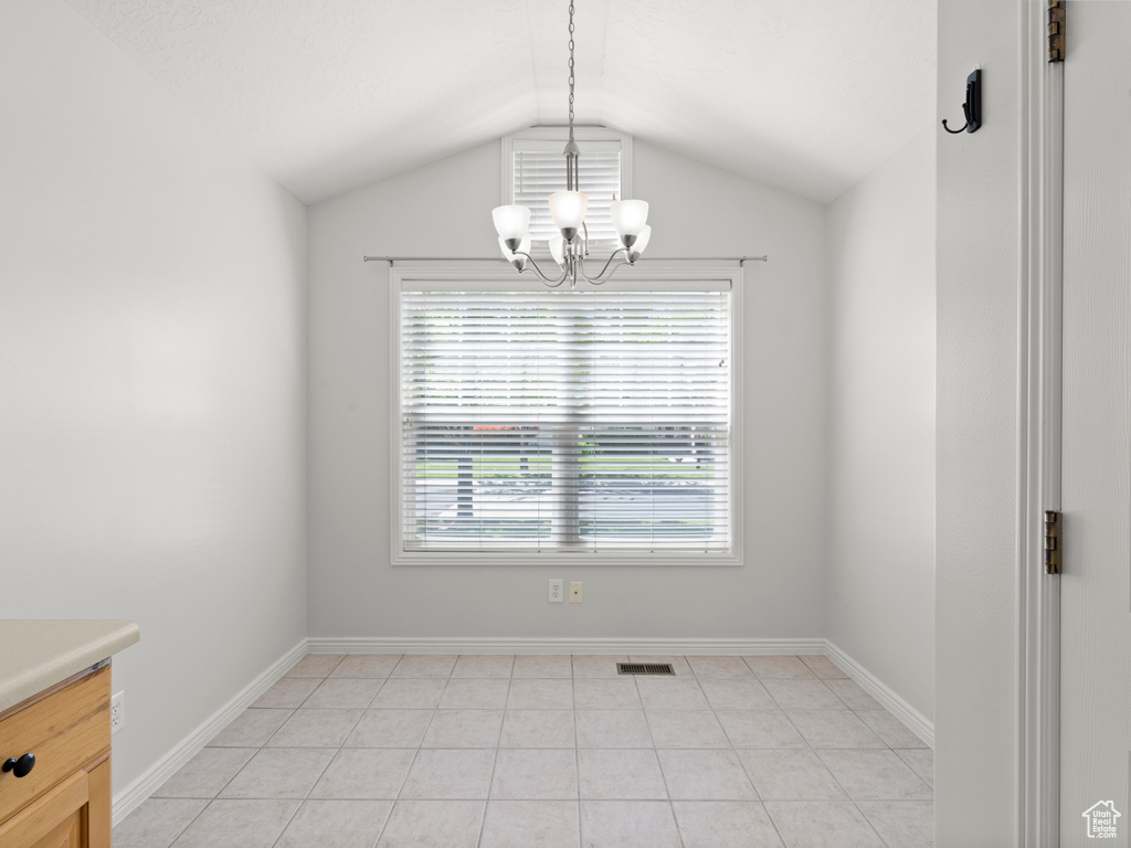 Unfurnished dining area featuring a chandelier, lofted ceiling, baseboards, and light tile patterned floors