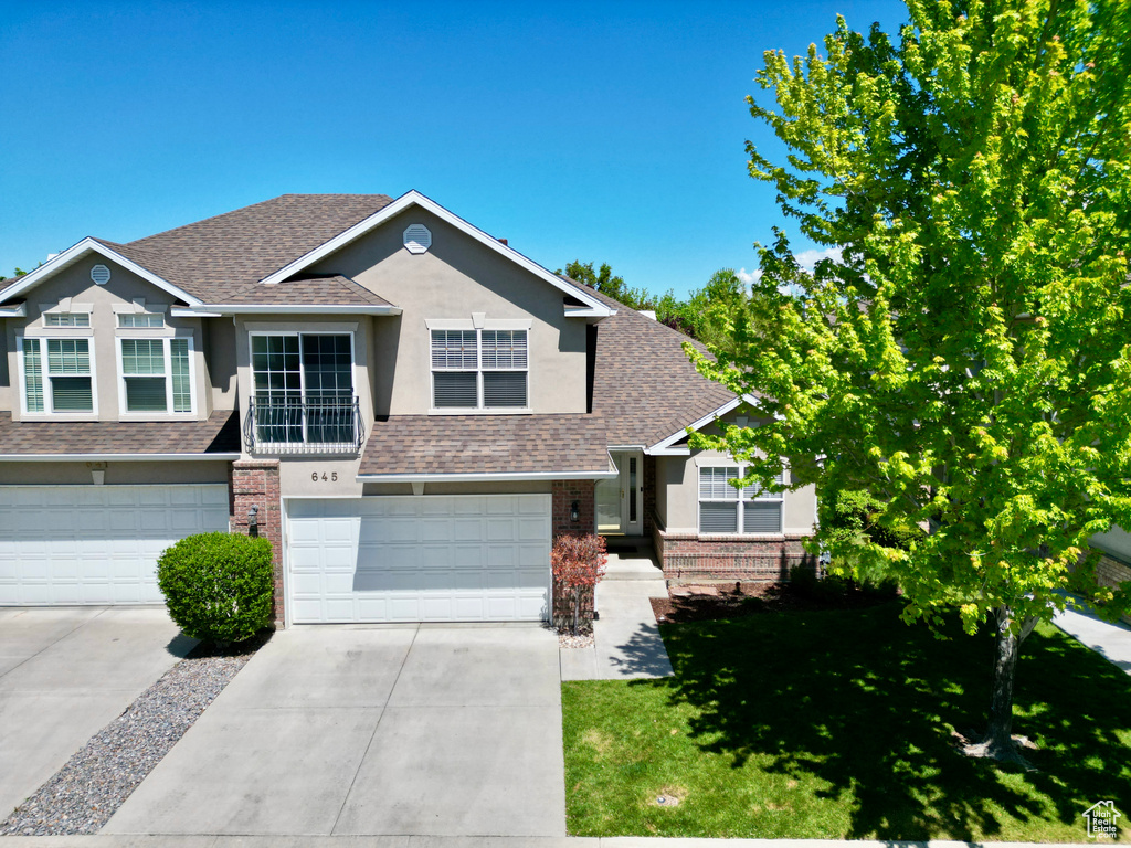 View of front of house featuring a shingled roof, brick siding, stucco siding, and driveway