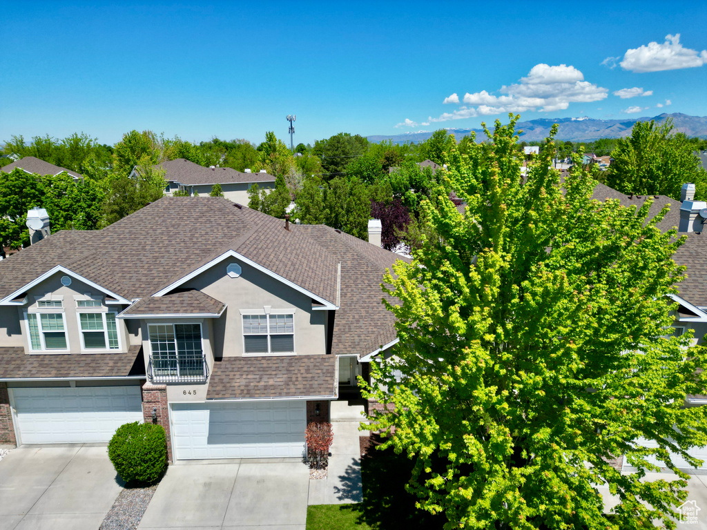 View of front facade featuring a shingled roof, a garage, concrete driveway, brick siding, and a mountain view
