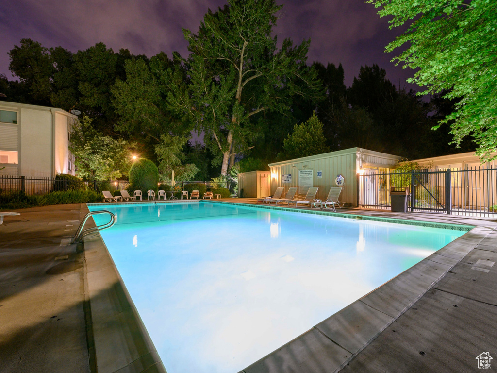 Pool at night featuring fence, a community pool, and a patio