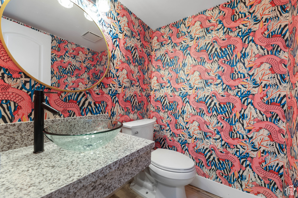 Half bathroom with wallpapered walls, toilet, and a sink