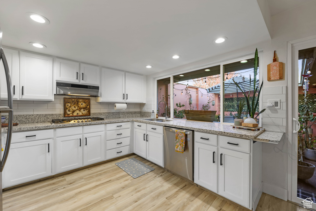 Kitchen with stainless steel appliances, under cabinet range hood, light wood-style flooring, decorative backsplash, and a sink