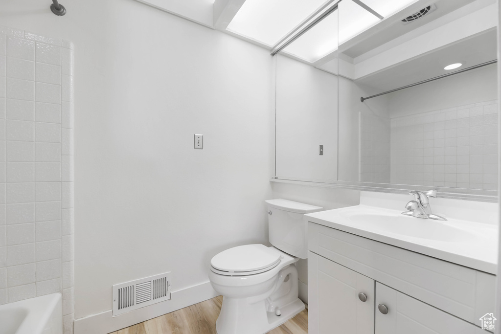 Bathroom featuring wood finished floors, toilet, vanity, baseboards, and shower / washtub combination