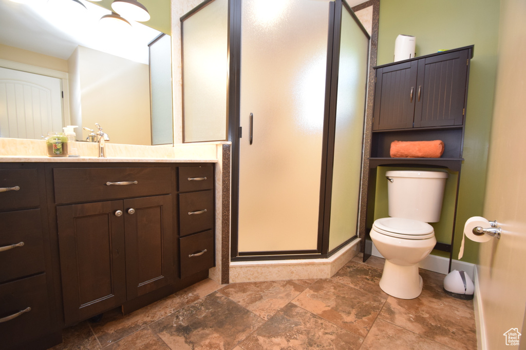 Bathroom with a shower stall, toilet, vanity, and stone finish floors