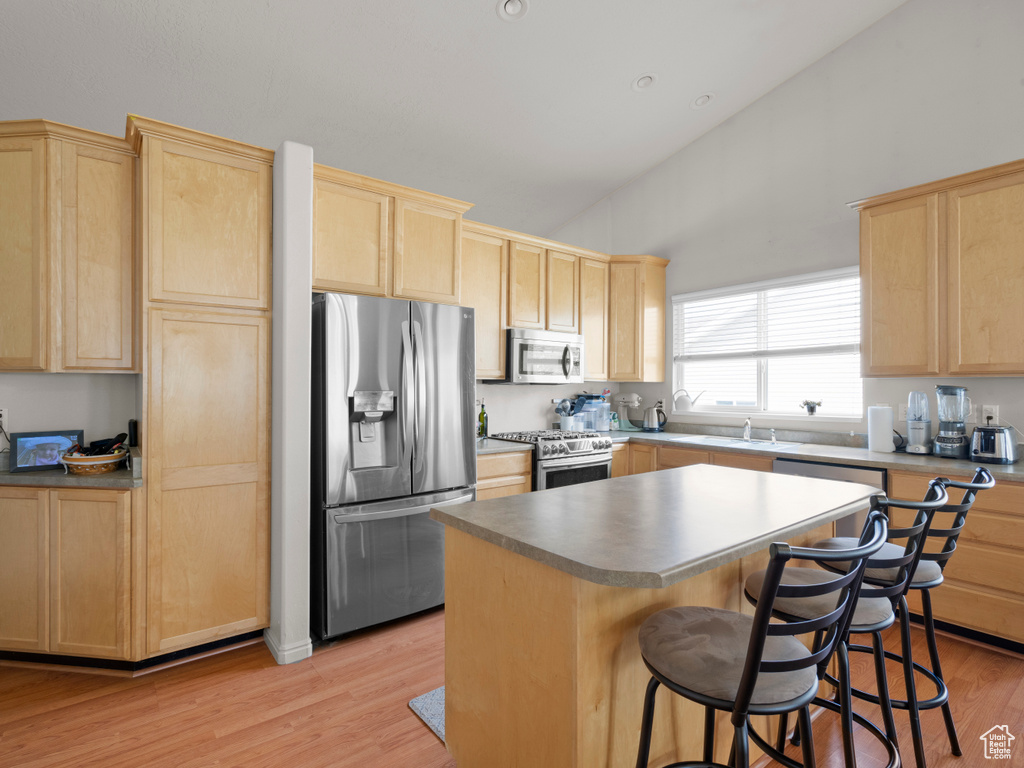Kitchen with stainless steel appliances, light brown cabinetry, a breakfast bar, light wood-style flooring, and a kitchen island