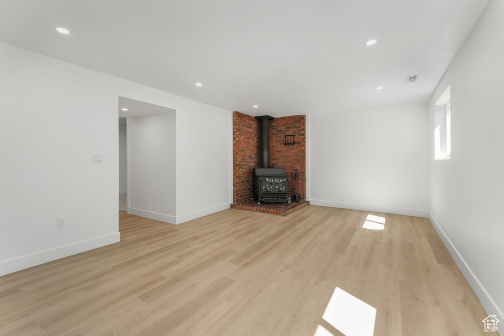 Unfurnished living room featuring a wood stove, light wood finished floors, baseboards, and recessed lighting