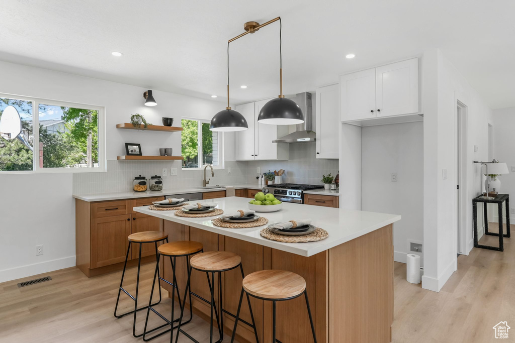 Kitchen featuring wall chimney exhaust hood, a sink, gas stove, light countertops, and recessed lighting