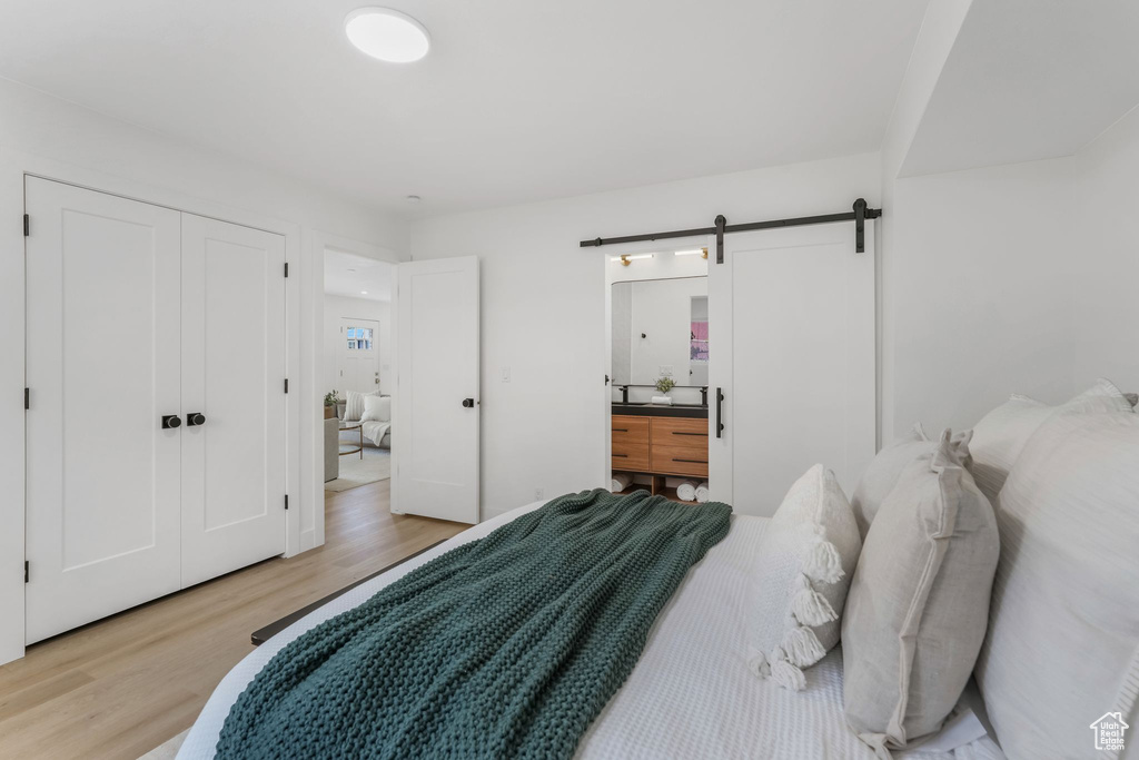 Bedroom with light wood finished floors, a barn door, and ensuite bathroom