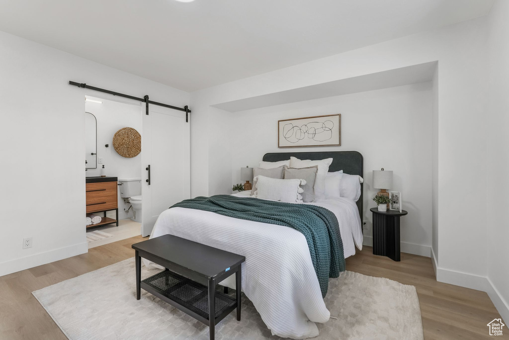 Bedroom with a barn door, wood finished floors, and baseboards