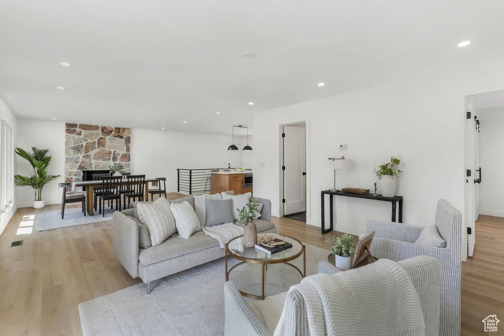 Living room with light wood finished floors, recessed lighting, a stone fireplace, and baseboards