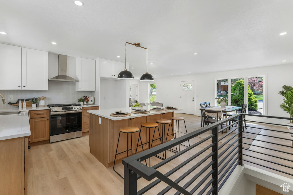 Kitchen with gas stove, wall chimney exhaust hood, light countertops, recessed lighting, and light wood-style flooring