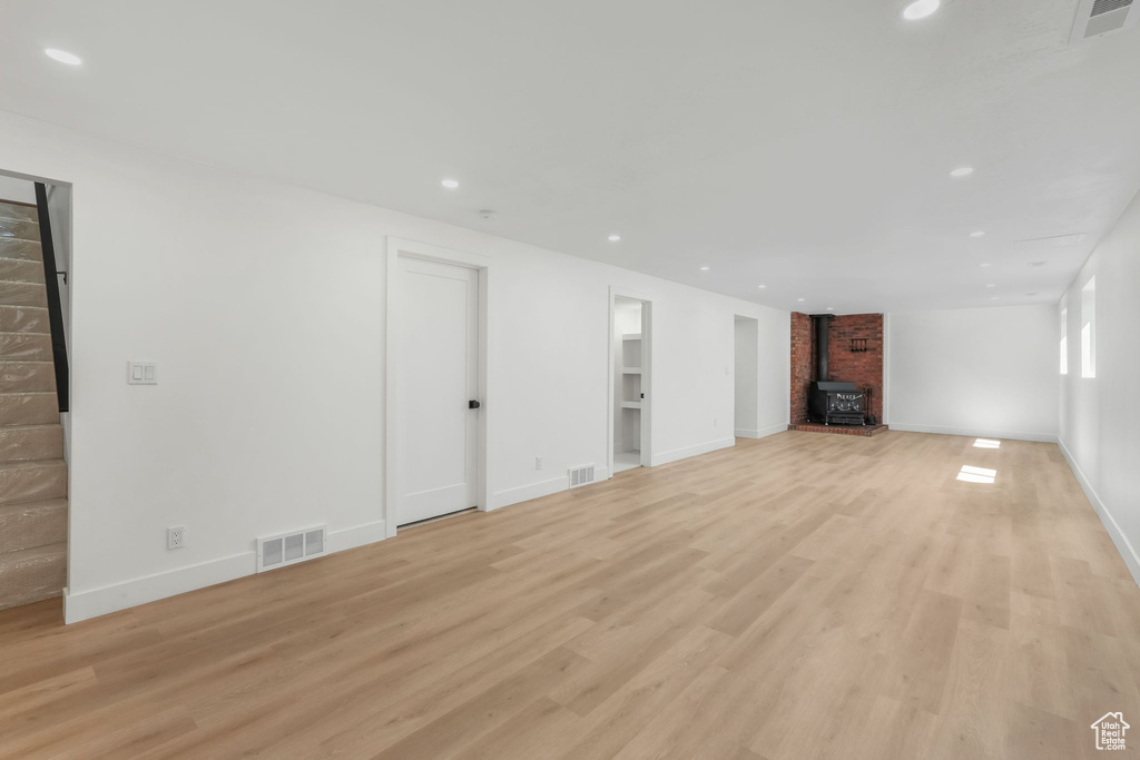 Unfurnished living room with a wood stove, light wood-type flooring, recessed lighting, and baseboards