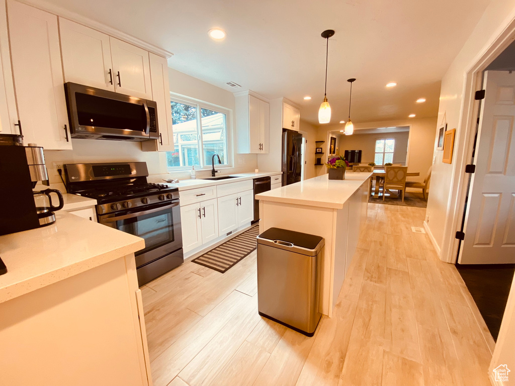 Kitchen with appliances with stainless steel finishes, a sink, light wood-type flooring, a center island, and light countertops