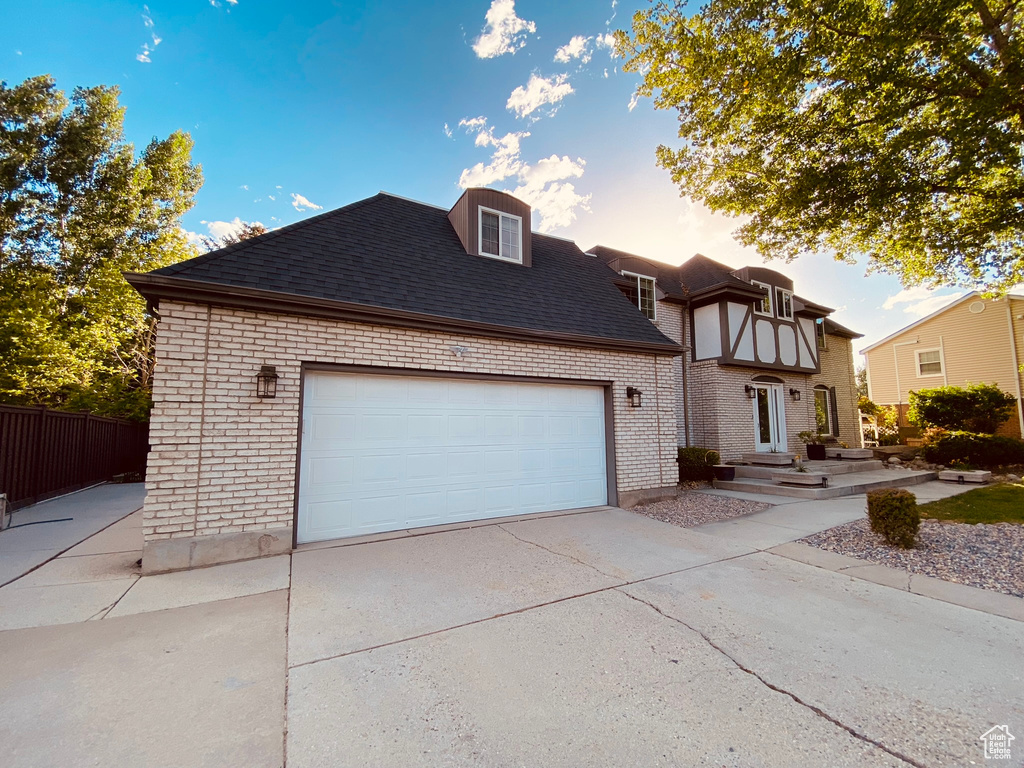 View of front of house with a shingled roof, concrete driveway, brick siding, and fence
