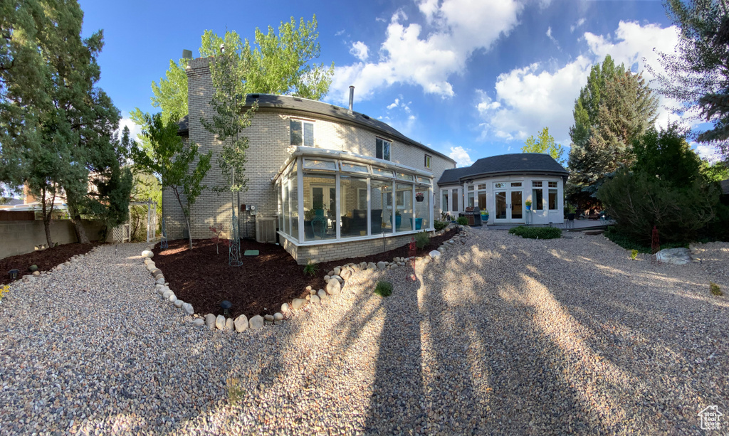 Back of house featuring a sunroom, french doors, a chimney, brick siding, and central AC unit