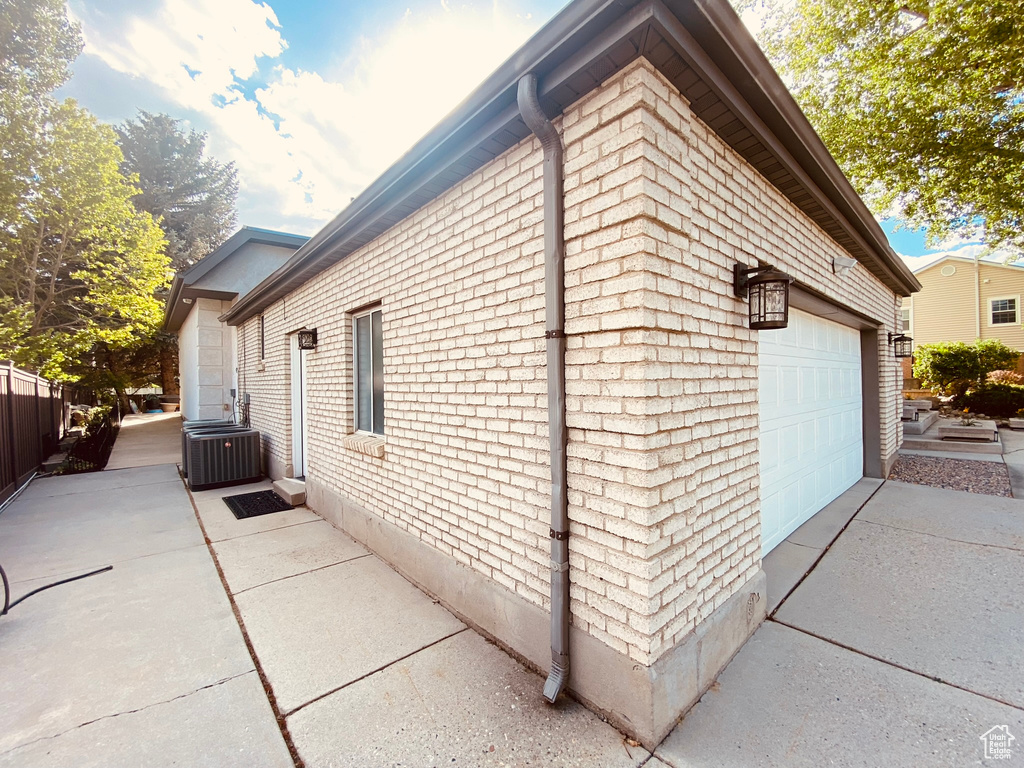 View of home\\\'s exterior featuring central AC unit, brick siding, a detached garage, and fence
