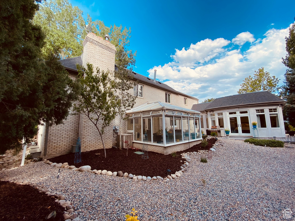 Rear view of property with a sunroom, french doors, a chimney, and roof with shingles