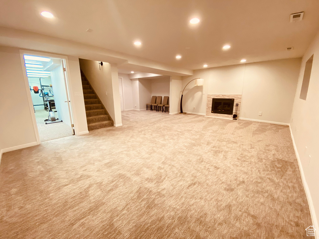 Finished basement with light colored carpet, recessed lighting, stairway, baseboards, and a fireplace with flush hearth