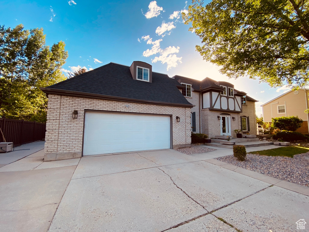 View of front of property featuring brick siding, driveway, fence, and an attached garage
