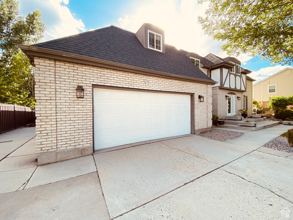 View of front of property featuring concrete driveway, roof with shingles, brick siding, and fence