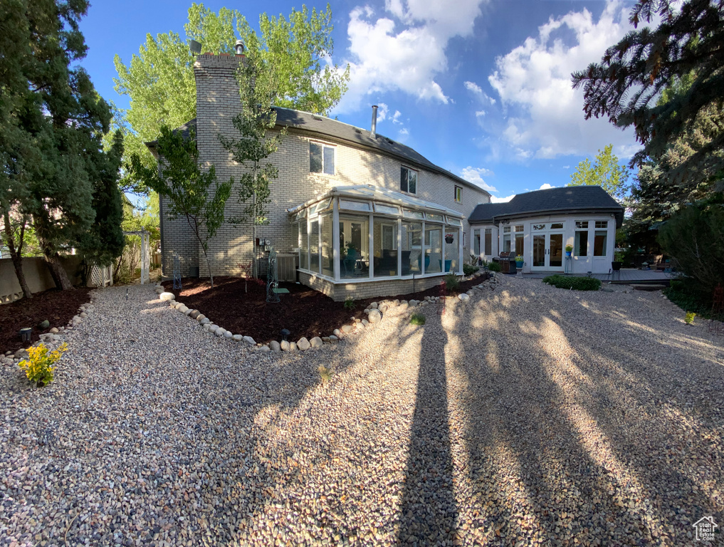 Back of house with a sunroom, french doors, a chimney, brick siding, and gravel driveway