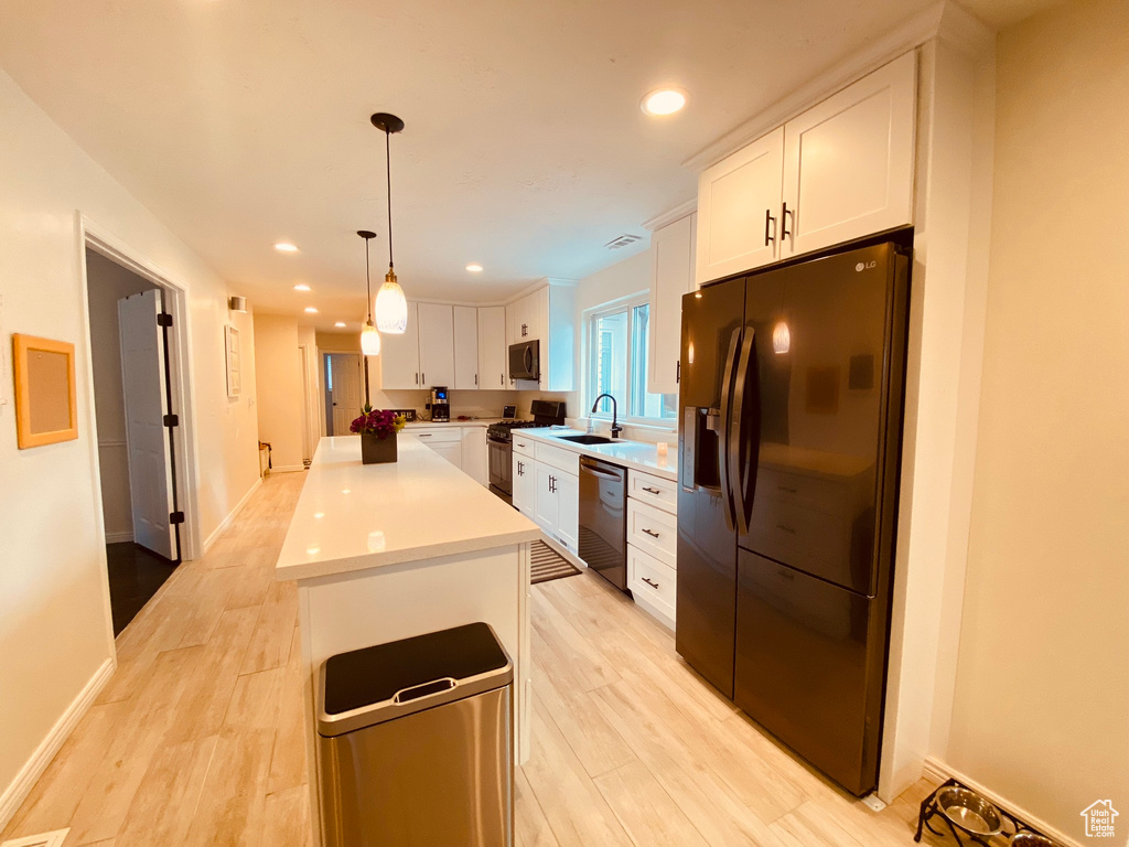 Kitchen with appliances with stainless steel finishes, a kitchen island, white cabinets, a sink, and light wood-type flooring