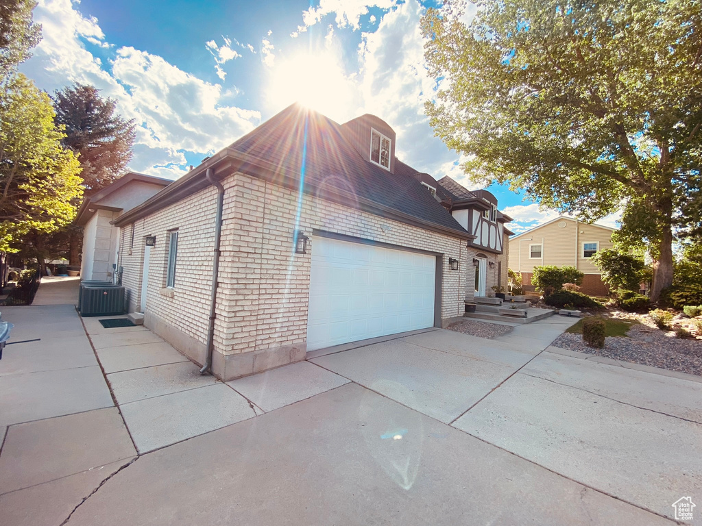 View of property exterior with central air condition unit, brick siding, concrete driveway, and a garage