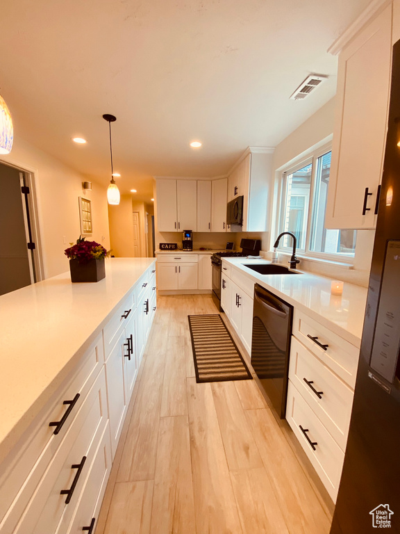 Kitchen featuring black appliances, light wood-type flooring, recessed lighting, pendant lighting, and white cabinetry
