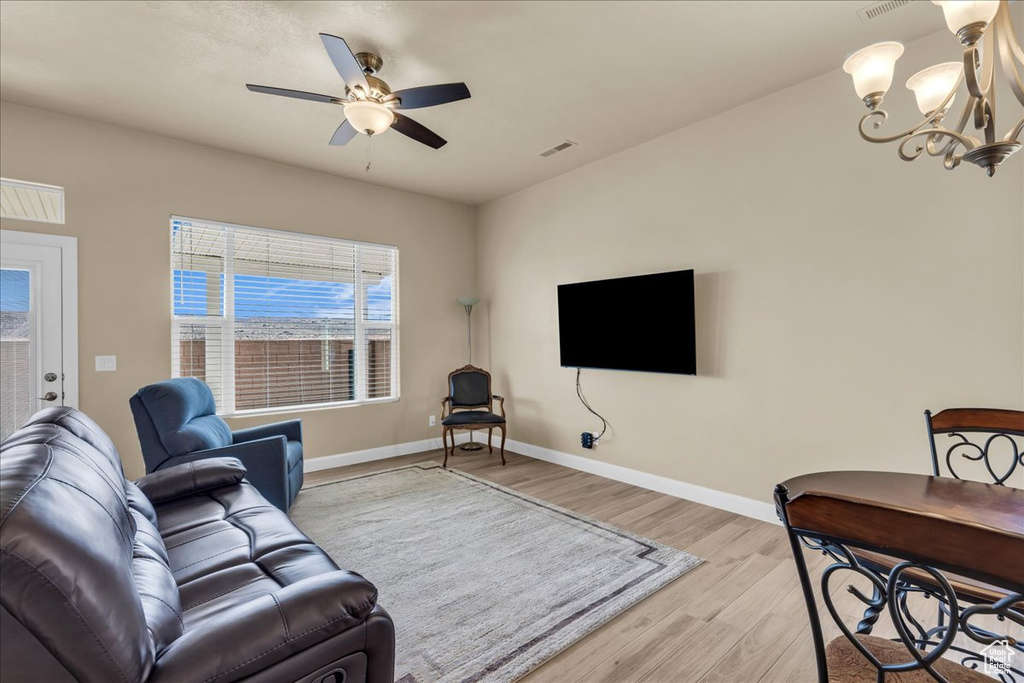 Living area with light wood finished floors, a chandelier, a ceiling fan, and baseboards