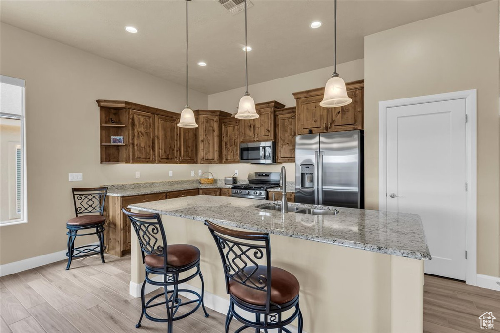 Kitchen with appliances with stainless steel finishes, open shelves, baseboards, light stone countertops, and a sink