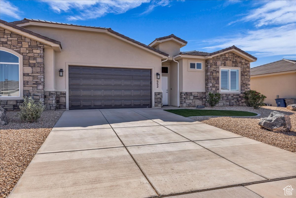 Single story home featuring stone siding, stucco siding, an attached garage, driveway, and a tile roof