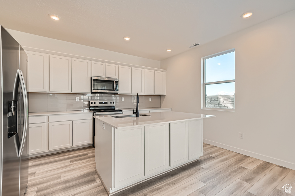 Kitchen featuring appliances with stainless steel finishes, a sink, light countertops, a kitchen island with sink, and recessed lighting