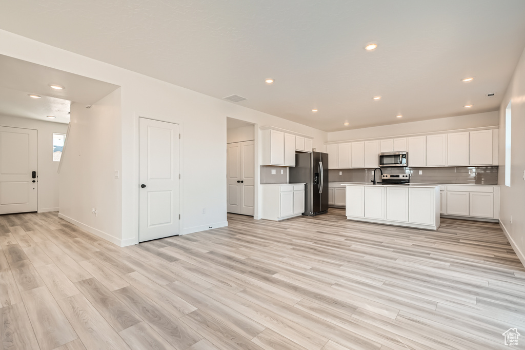 Kitchen with appliances with stainless steel finishes, light wood-style flooring, white cabinetry, open floor plan, and recessed lighting