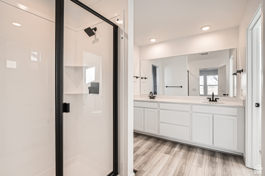 Full bathroom featuring a stall shower, double vanity, wood finished floors, and recessed lighting