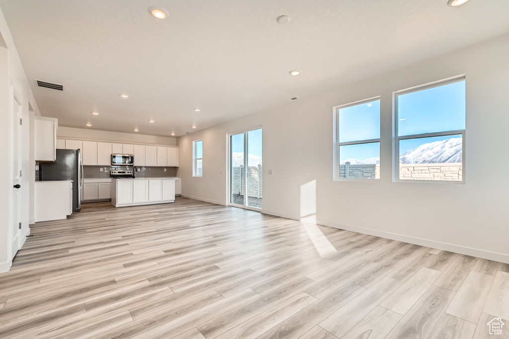 Unfurnished living room with recessed lighting, light wood-style floors, and baseboards