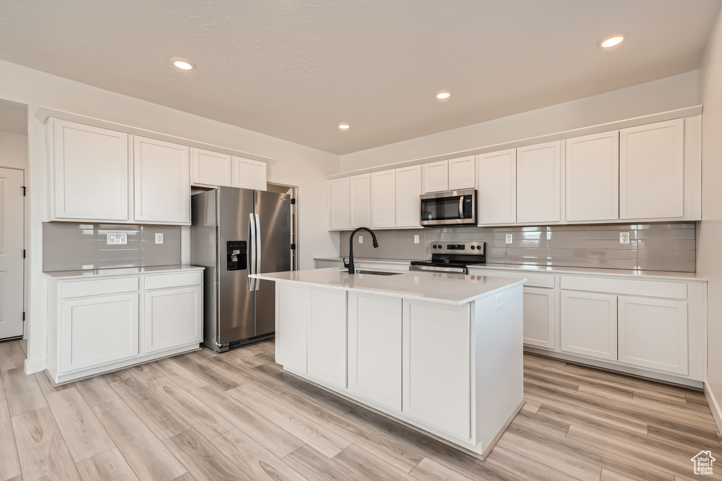 Kitchen featuring stainless steel appliances, a sink, light countertops, backsplash, and white cabinetry