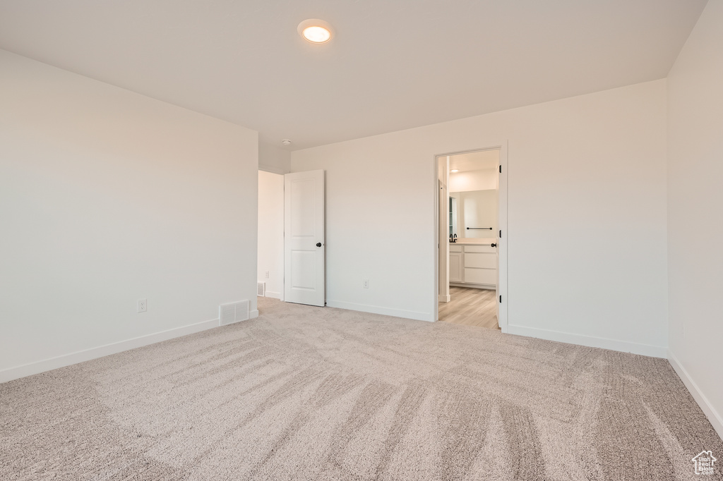 Unfurnished bedroom featuring light colored carpet, baseboards, and ensuite bath
