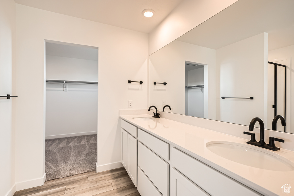 Full bathroom featuring wood finished floors, double vanity, a spacious closet, a shower with shower door, and recessed lighting
