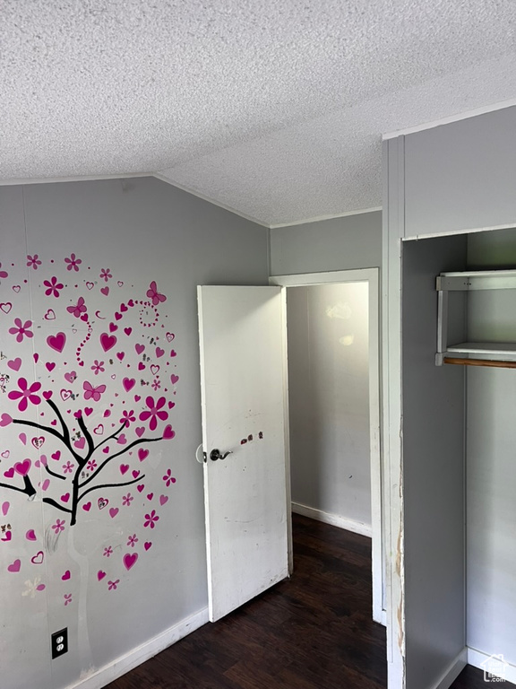 Unfurnished bedroom with wood finished floors, a closet, lofted ceiling, a textured ceiling, and baseboards