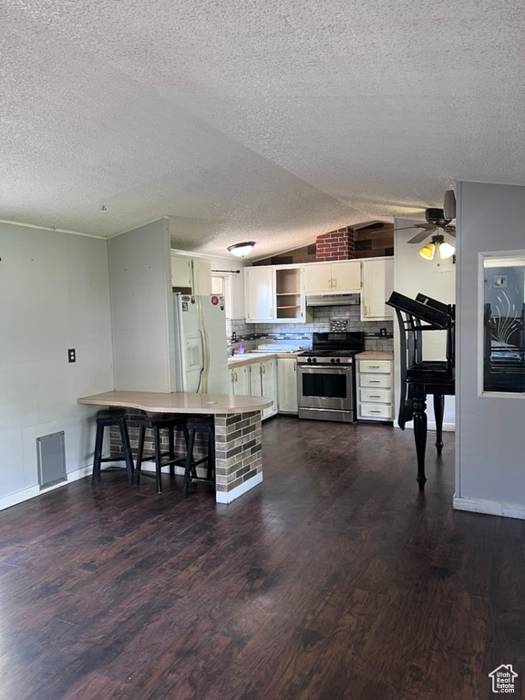 Kitchen featuring stainless steel range oven, white refrigerator with ice dispenser, dark wood-style flooring, lofted ceiling, and under cabinet range hood