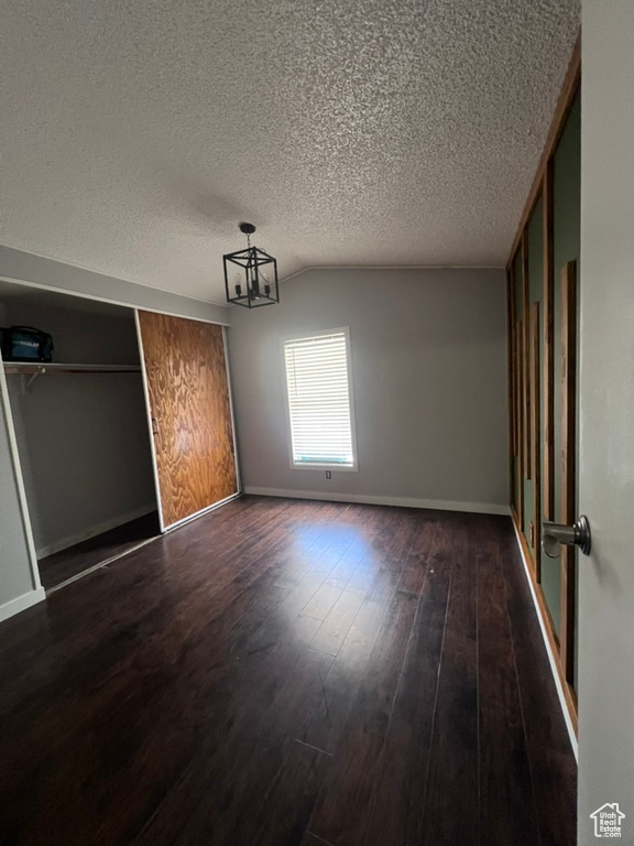 Unfurnished bedroom with dark wood-style floors, a textured ceiling, baseboards, a closet, and lofted ceiling
