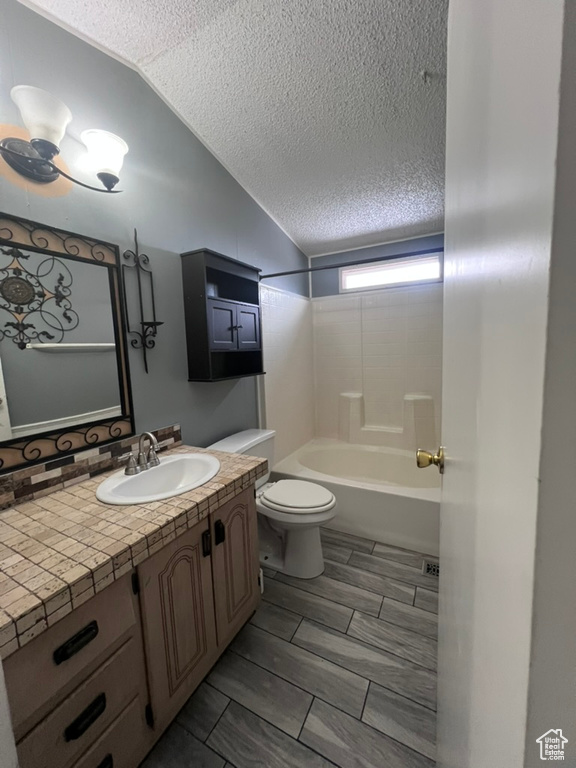 Full bath with toilet, a textured ceiling, vanity, vaulted ceiling, and shower / bathtub combination