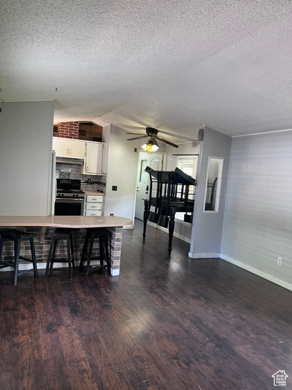 Kitchen featuring stainless steel gas stove, a textured ceiling, dark wood-style floors, ceiling fan, and white cabinetry
