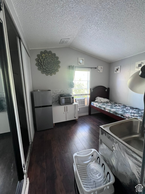 Bedroom with freestanding refrigerator, dark wood-style flooring, lofted ceiling, a textured ceiling, and a closet